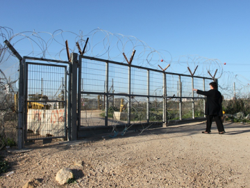 A woman describes the pain and injustice she feels at being cut off from her lands. This is a farmers gate. This gate only opens 3 times a day and a permit is required to pass through it. On the other side are Palestinian lands. If a family is granted a permit to tend their lands only one person will be allowed to cross for a limited period of time. The system has no regard for land rights or the size of the land. As a result many families who were at one time self-sufficient are now facing a life of poverty. Also many Palestinians fear that if their land is left unattended it will be defined uncultivated and after 3 years become 'state land'. Palestinians have no way to protect their lands from this.